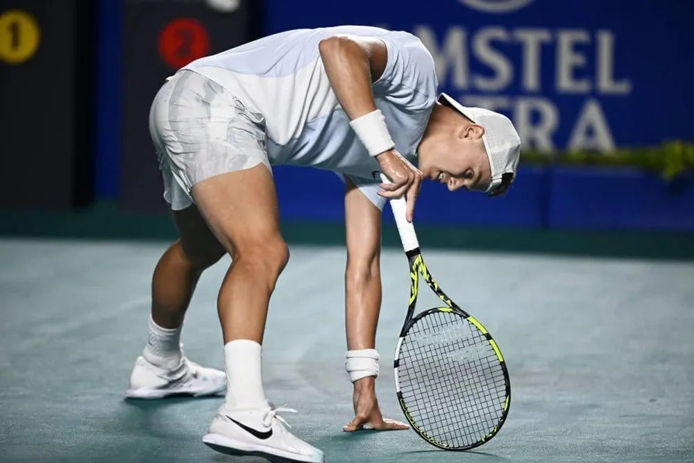 Holger Rune balances on his tennis racket, held in his right hand, after slipping on a tennis court.